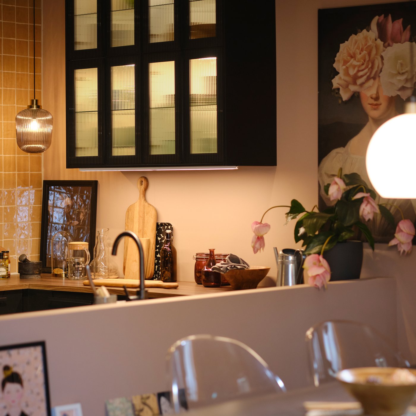 A kitchen with wall cabinets with glass doors and lighting inside, plus pendant lamps over the worktop and extendable table.