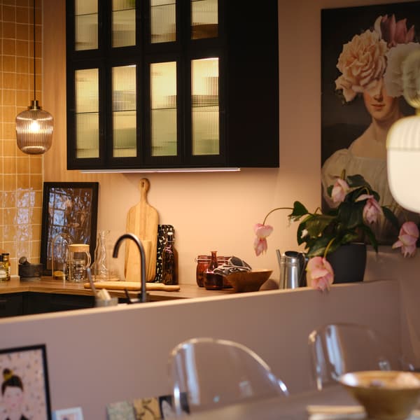 A kitchen with wall cabinets with glass doors and lighting inside, plus pendant lamps over the worktop and extendable table.