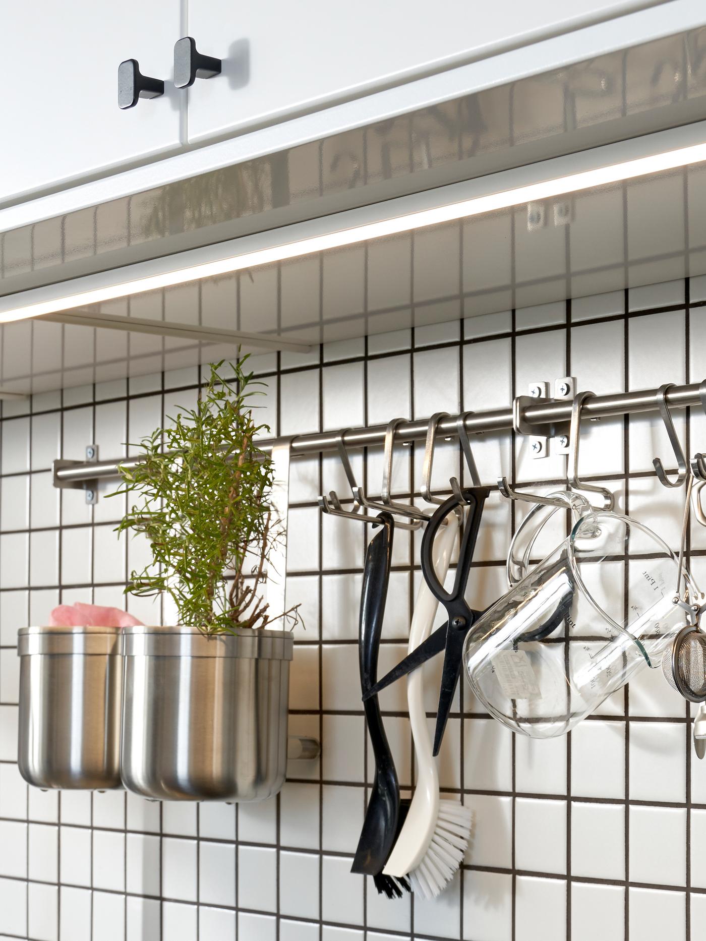 A kitchen with white cabinet doors. A white tile wall with a mounted rail and hooks in stainless steel is underneath.