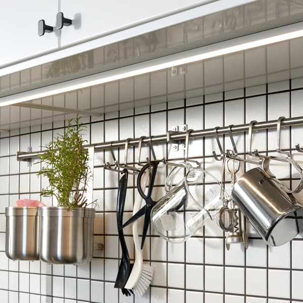 A kitchen with white cabinet doors, and under them is a white tile wall with a mounted rail and hooks in stainless steel.