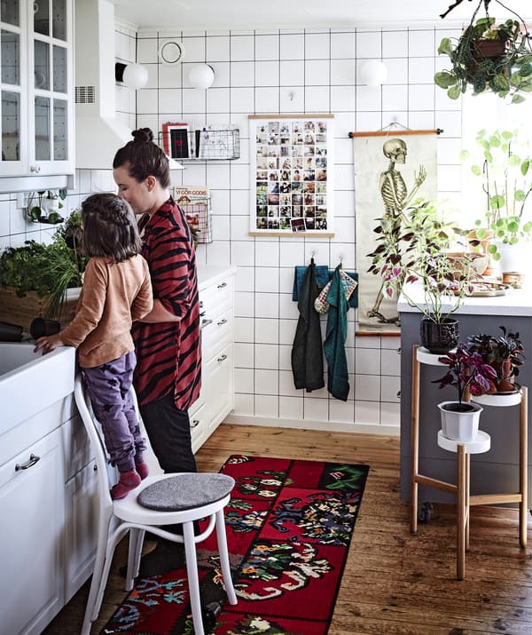 A kitchen with white units, hanging tea towels and a plant stand.