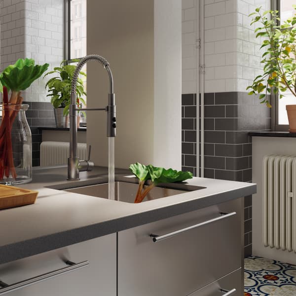A kitchen worktop, an inset sink and a mixer tap with handspray. The handspray washes rhubarb that lays in the inset sink.