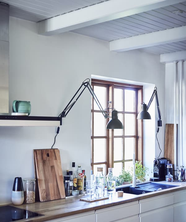 A kitchen worktop and sink, lined with cooking equipment and with lamps directing light over the sink area.