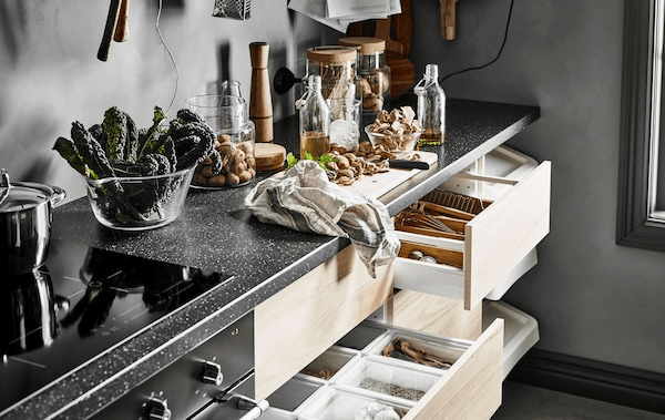 A kitchen worktop with a cutting board and clear glass storage jars and several open drawers with ash fronts 