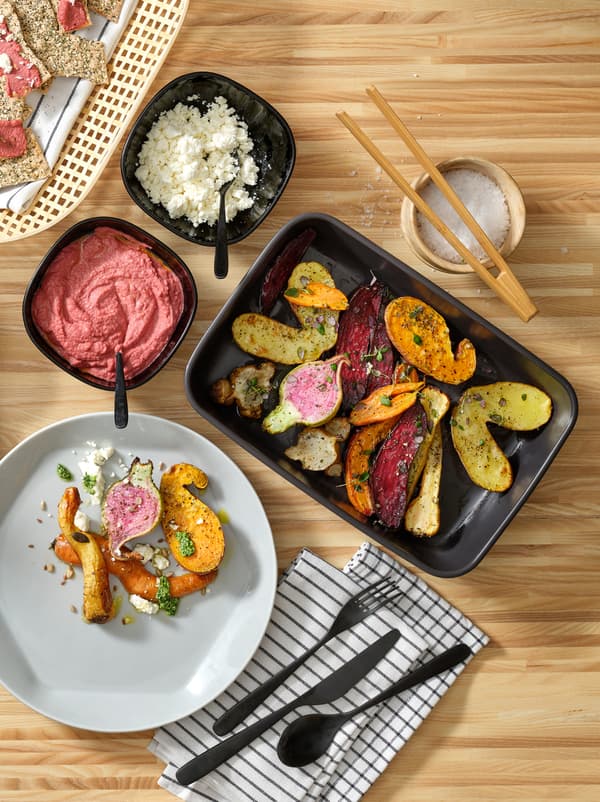 A kitchen worktop with a gray FORMIDABEL plate in a round yet hexagonal shape and colourful food in black serving dishes.