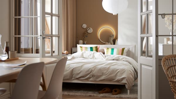 A KLEPPSTAD bed with light grey-beige ÄNGSLILJA bed linen stands beside a window in a small bedroom.