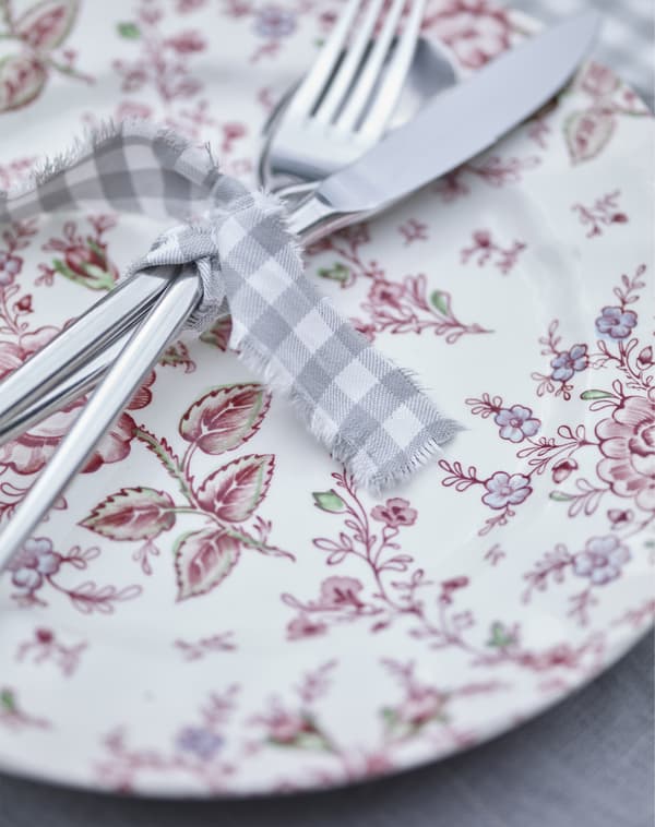 A knife and fork tied with some grey gingham string on a red patterned plate.