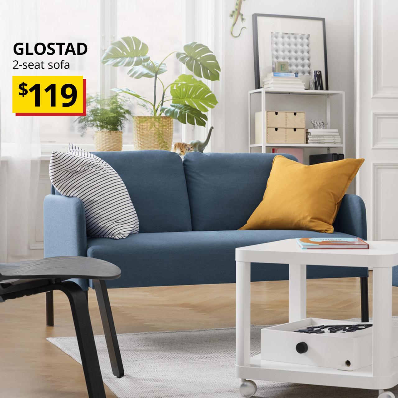 A knisa medium blue GLOSTAD 2-seater sofa in a living room setting next to a black stained oak veneer FRÖSET easy chair and a white TINGBY side table on castors. At the top left of the image, black text over the image reads "GLOSTAD, 2-seat sofa." BTI Price: $119.