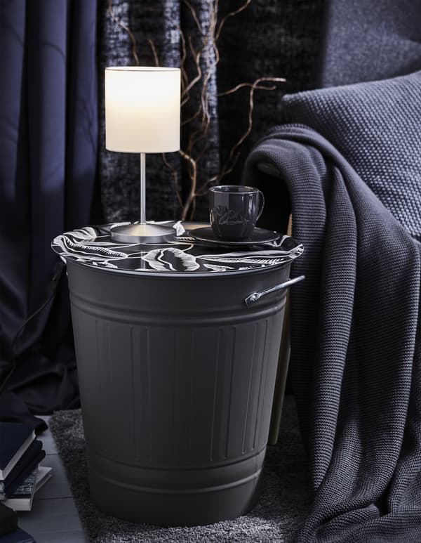 A KNODD bin is topped with a decorative tray to create a side table, and has a lamp and cup of coffee resting on it.