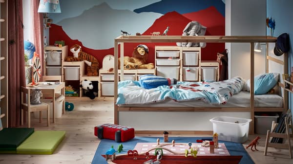 A KURA reversible bed stands in a children’s room with a mountain scene painted on the wall and lots of toys everywhere.