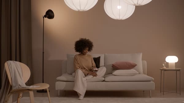 A lady is sitting on a sofa in the living room with various types of lighting around her.