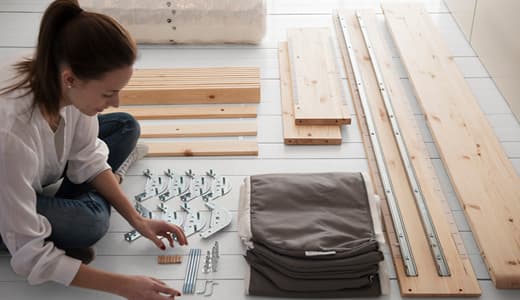A lady sitting on the floor, laying out all the parts of an IKEA bed to be assembled. 