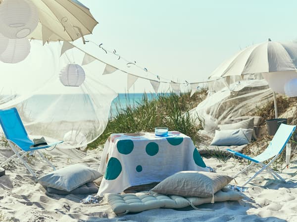 A laidback party with umbrellas, cushions and foldable chairs is set up on the beach.