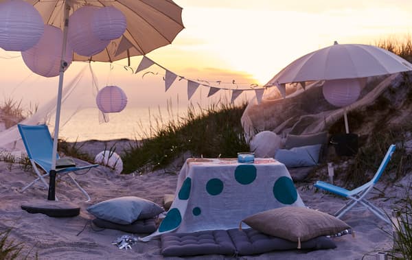 A laidback party with umbrellas, cushions and foldable chairs is set up on the beach.