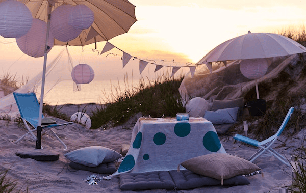 A laidback party with umbrellas, cushions and foldable chairs is set up on the beach.