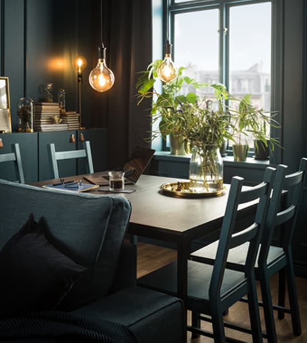 A laptop, notebook, and glass vase with greenery sits on a dining table.