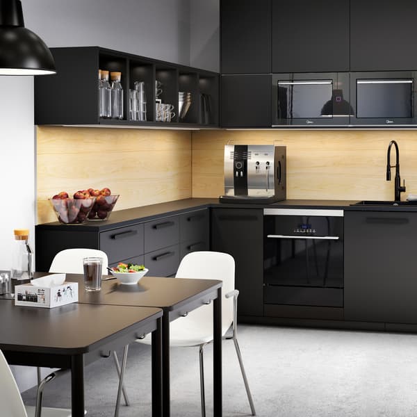 A large anthracite kitchen with drawers and cabinets, coffee machine, bowls with fruits and two tables with white chairs.