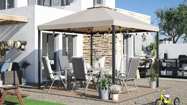 A large backyard with a dining table, outdoor chairs with cushions, a gazebo, wood-like decking and an outdoor kitchen.