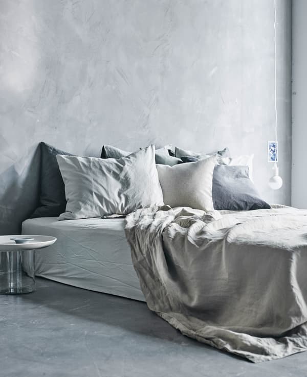 A large bed, low to the floor, covered in light coloured textiles.