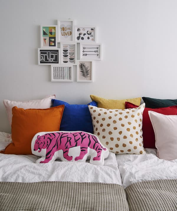 A large bed with lots of colourful cushions and a collage frame of pictures on the wall.