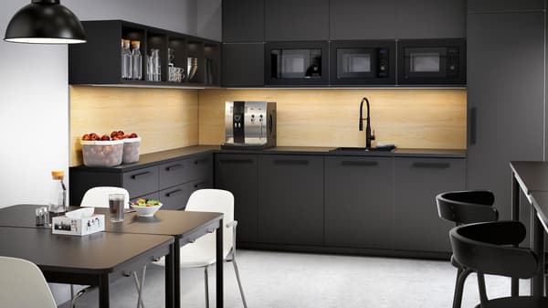 A large black kitchen with drawers and cabinets, coffee machine, bowls with fruits and two tables with white chairs.