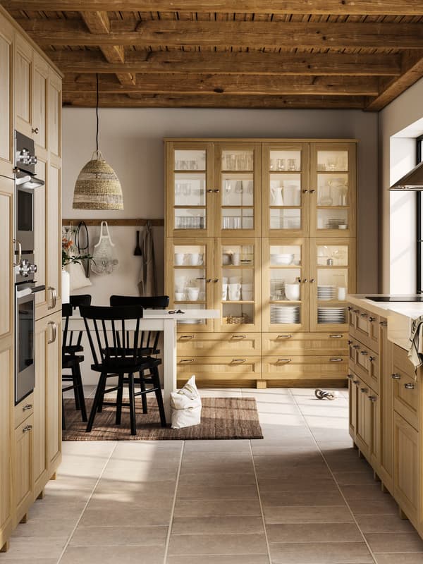 A large, bright kitchen with oak VEDHAMN fronts, including glass door cabinets filled with glassware and dinnerware.
