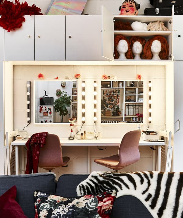 A large dressing table with two pink chairs and two mirrors with lights around the edges.