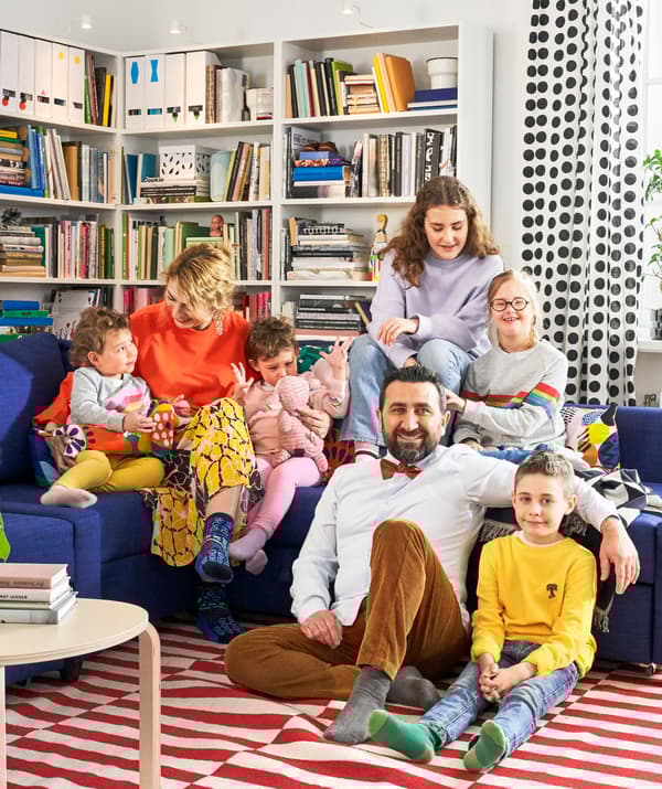 A large family sitting on a blue FRIHETEN corner sofa with bookshelves behind them.