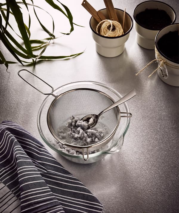 A large glass bowl under an IDEALISK strainer, with the wet paper pulp from the napkins, together with three planters.