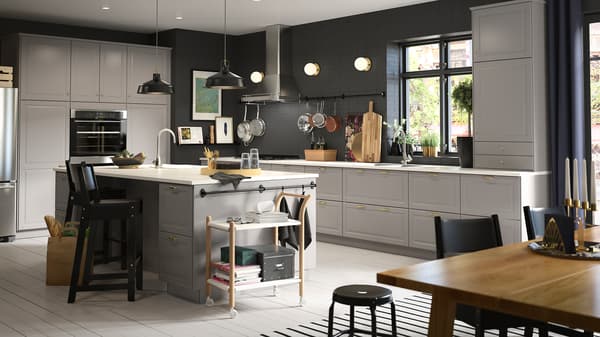A large gray kitchen with an island in the center, two black bar stools with backrests and two black pendant lamps.