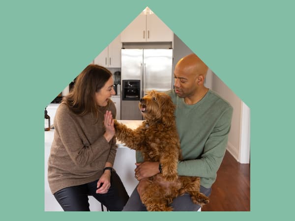 A large house shape with image of a young couple sitting in their kitchen laughing and playing with their small dog.
