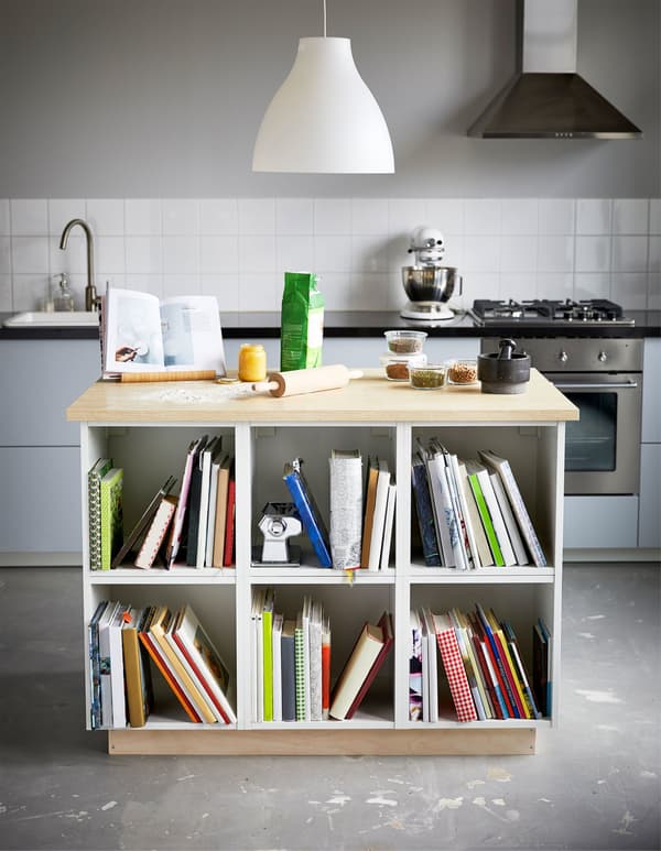 A large kitchen island is used for baking on top and holds lots of cookbooks on the shelves below.