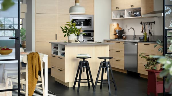 A large kitchen island with ASKERSUND fronts in light ash effect has two black stools and a white pendant lamp above it.