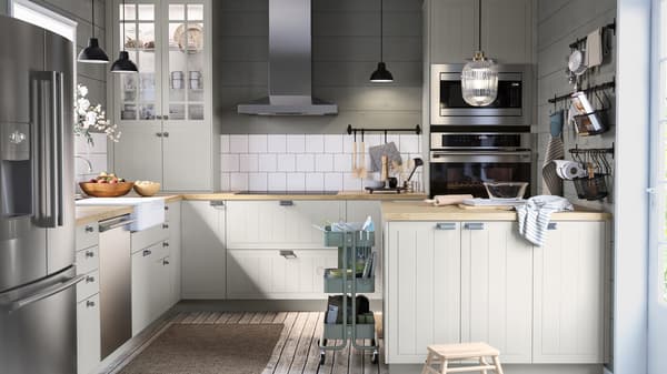 A large kitchen with green and white walls, a kitchen island with bakeware, black rails with hooks, a trolley.