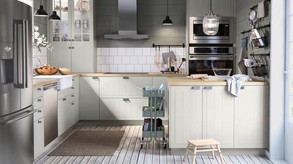 A large kitchen with green and white walls, a kitchen island with bakeware, black rails with hooks, a trolley.