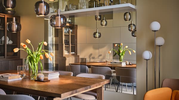 A large MÖRBYLÅNGA table sits in the center of a narrow yet sophisticated dining room with plenty of mirrors on one wall.