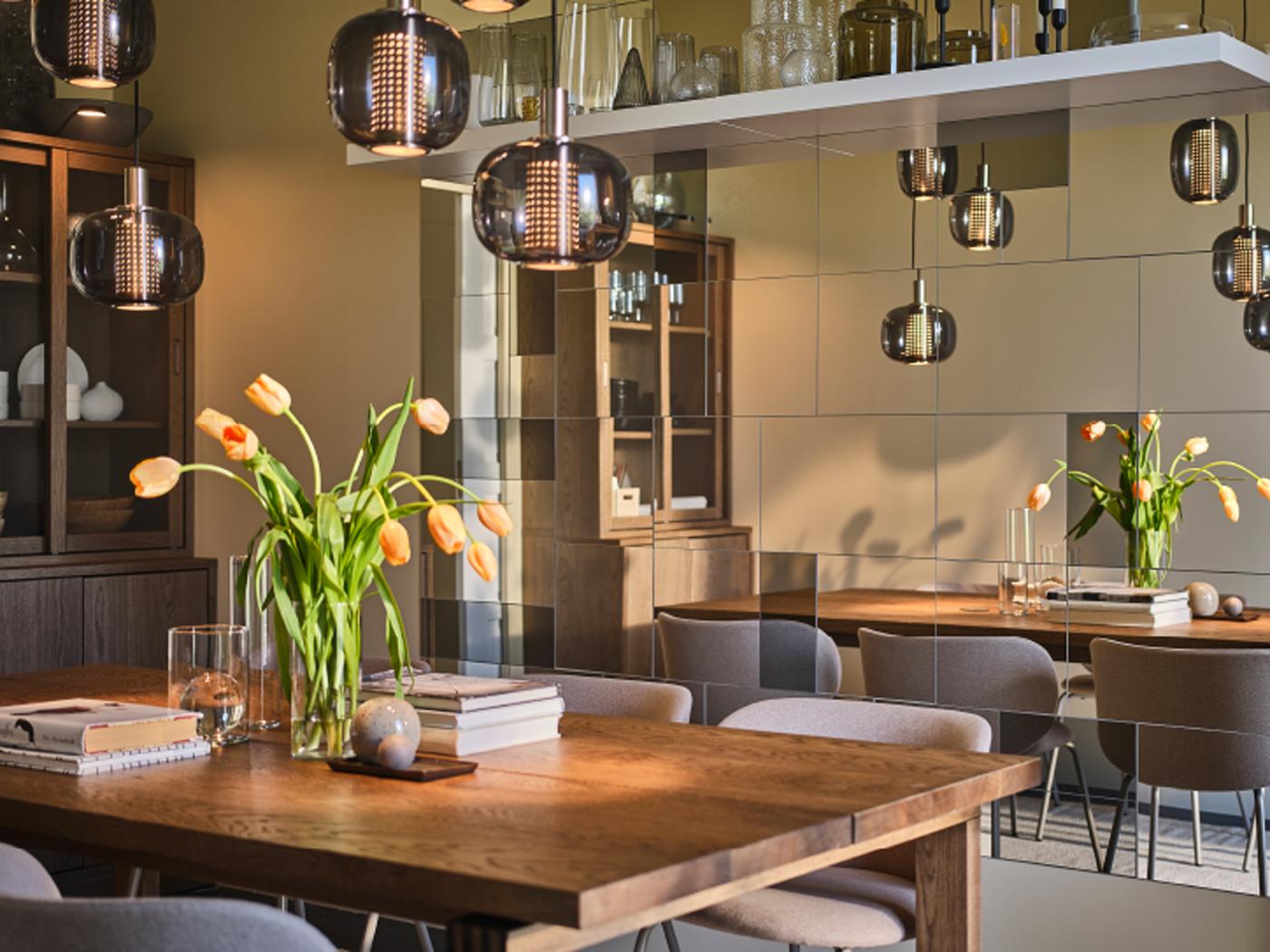 A large MÖRBYLÅNGA table with vases, flowers and books on top stands in a dining room with plenty of mirrors on one wall.