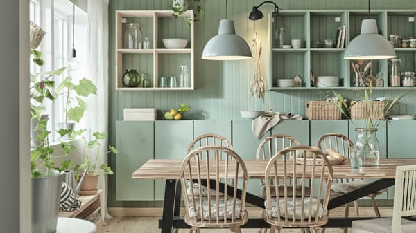 A large SKOGSTA dining table in wood with four matching chairs and one white children’s chair, a glass vase with flowers.