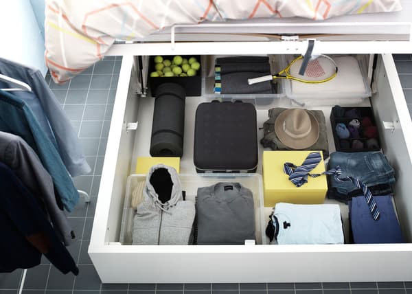 A large underbed storage compartment full of clothes, IKEA suitcase and sports gear.