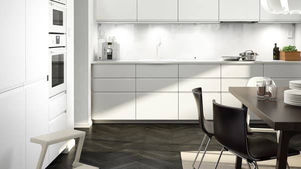 A large white kitchen with matt white kitchen doors and drawer fronts, a white worktop and a dark brown table with two chairs.