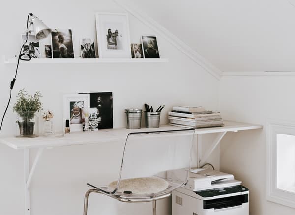 A large white shelf mounted to the wall and used as a home office desk worktop against a slanted wall to maximize space.