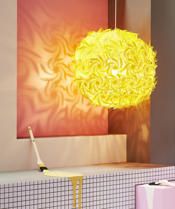 A large yellow pendant lamp with cut-out designs casting a decorative shadow against a red wall.