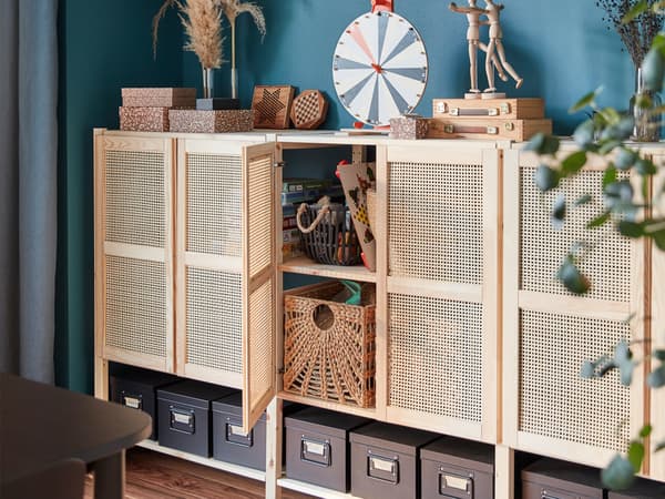 A lattice-fronted wall storage unit with one door open and storage boxes inside, plus storage boxes and accessories on top.