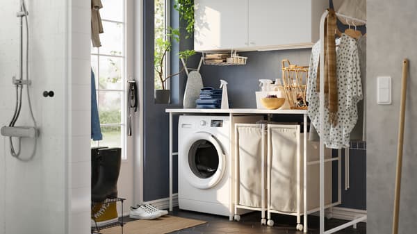 A laundry room with blue walls and a white ENHET storage combination, a washing machine and two laundry baskets on castors.