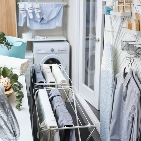 A laundry room with clothes drying on racks, an ironing board and a washing machine.