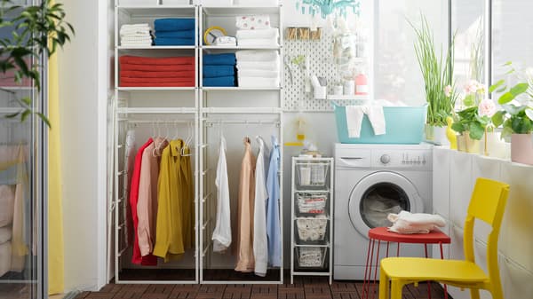 A laundry room with towels and clothes on a JONAXEL white shelving unit and a washing machine next to it.