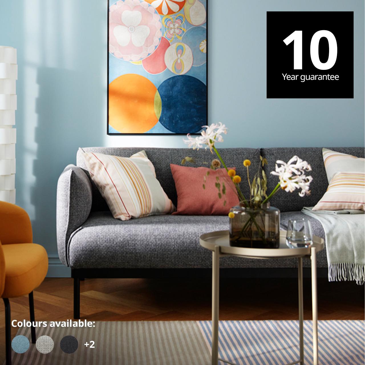 A leige grey with black frame ÄPPLARYD 3-seater sofa in a colourful yet sparsely furnished living room with a single art piece in a black LOMVIKEN frame on a light-blue wall. A 10-year guarantee tag is placed over the image at the top right corner. White text overlay image that reads "Colours available:" with the colour swatch of Hallarp beige, Hallarp grey and Saxemara black-blue.