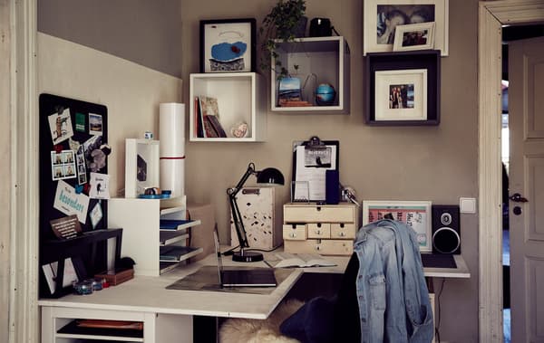 A letter tray and boxes on a corner desk with cubed storage units on the wall above.