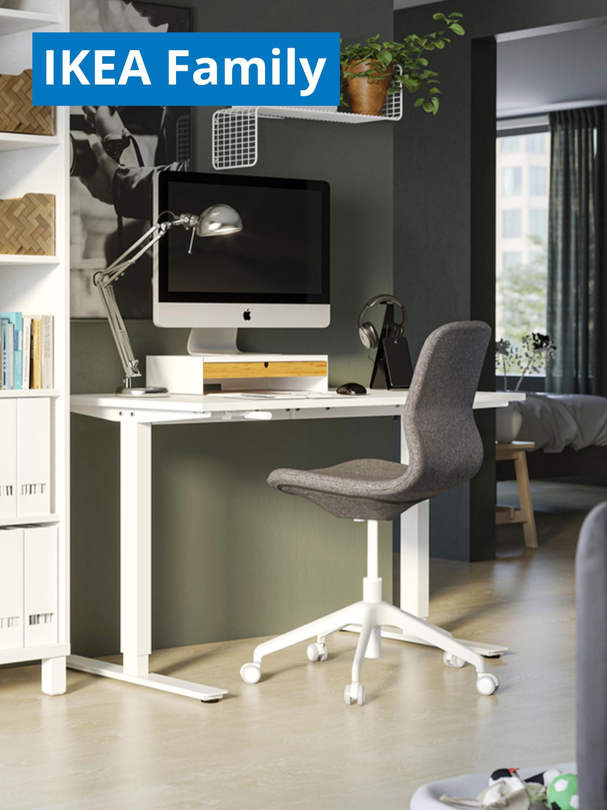 A lifestyle image of a white TROTTEN desk sit/stand with a grey/white office chair. On the top left corner, a blue tag with white text that reads "IKEA Family price".