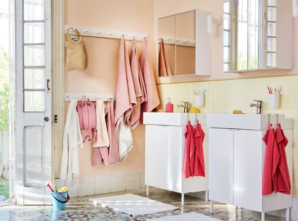 A light bathroom setting with various towels in both pink and coral, and bags hanging on the wall.